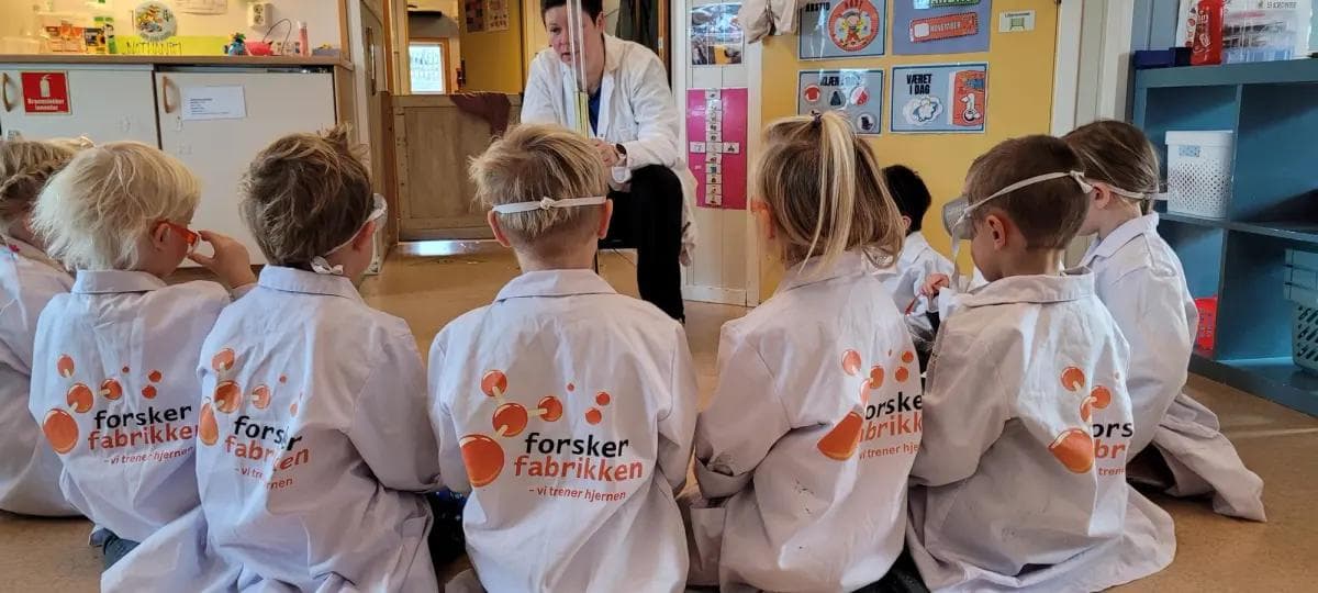 a group of children wearing lab coats are sitting on the floor .
