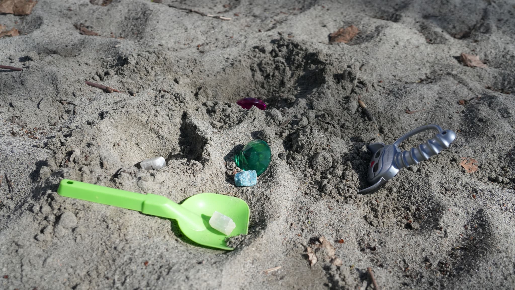 a green shovel and a green bottle are in the sand on the beach .
