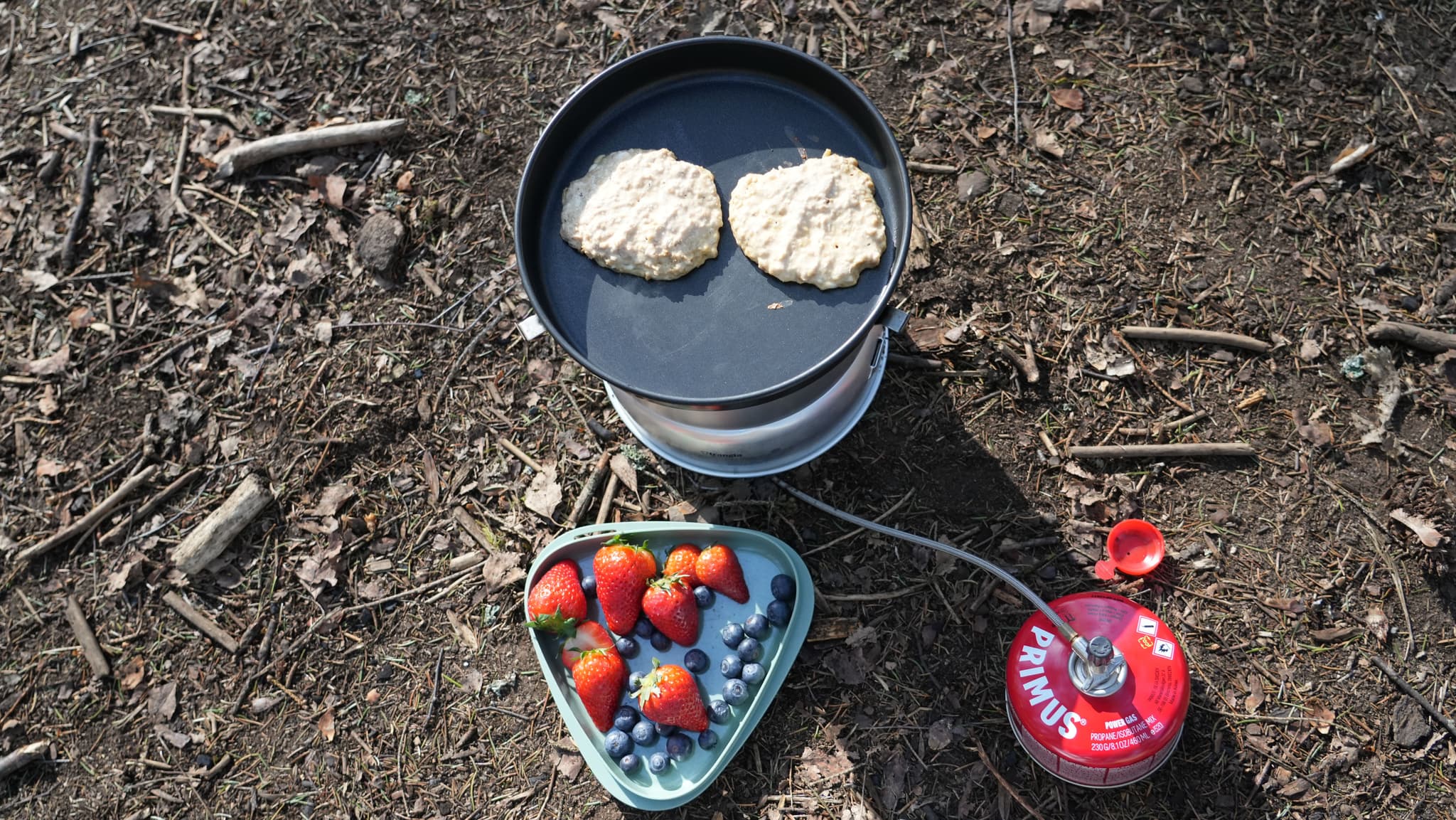 pancakes are being cooked on a stove next to a plate of strawberries and blueberries .