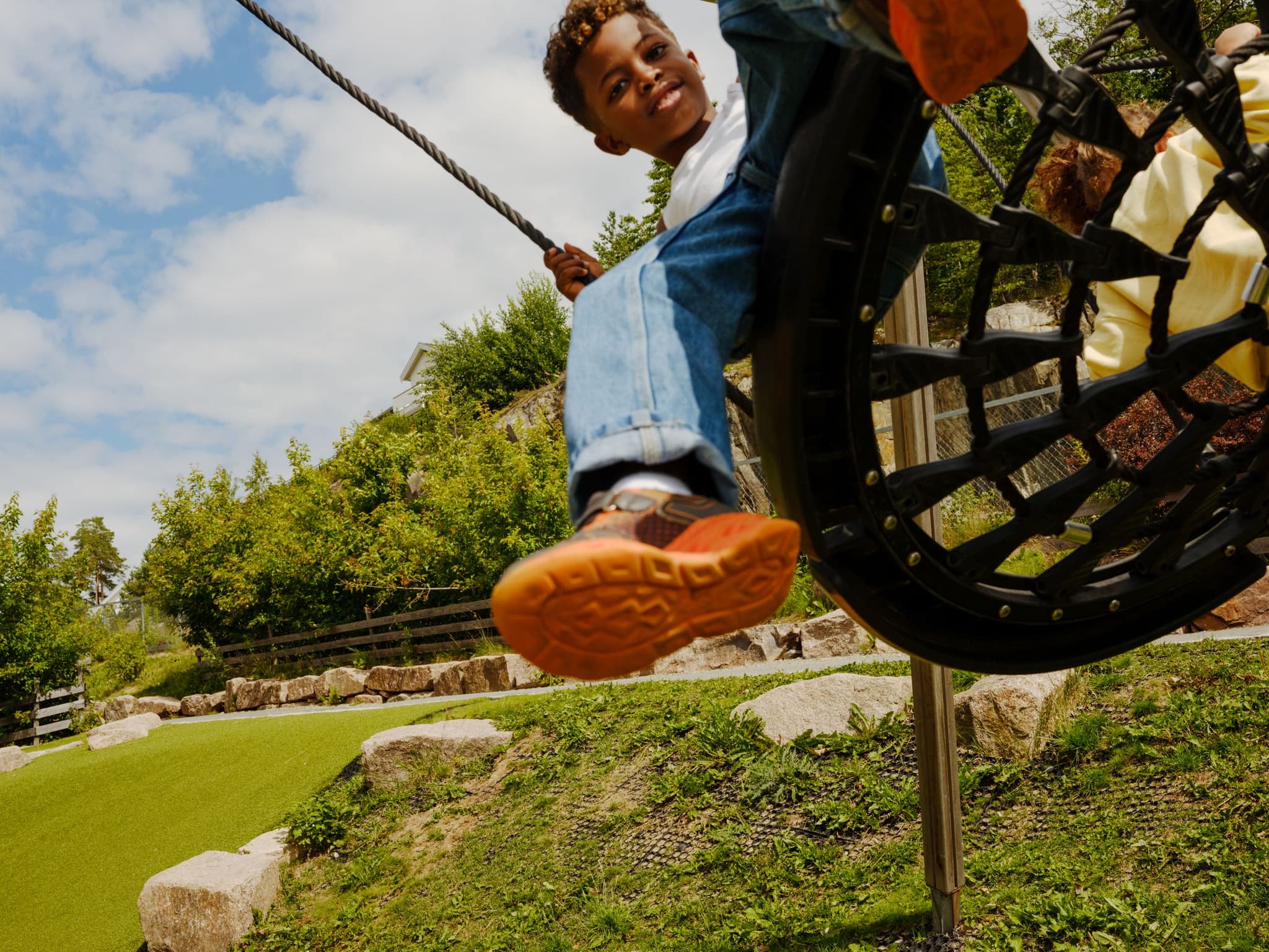 a young boy is riding a rope swing at a playground .