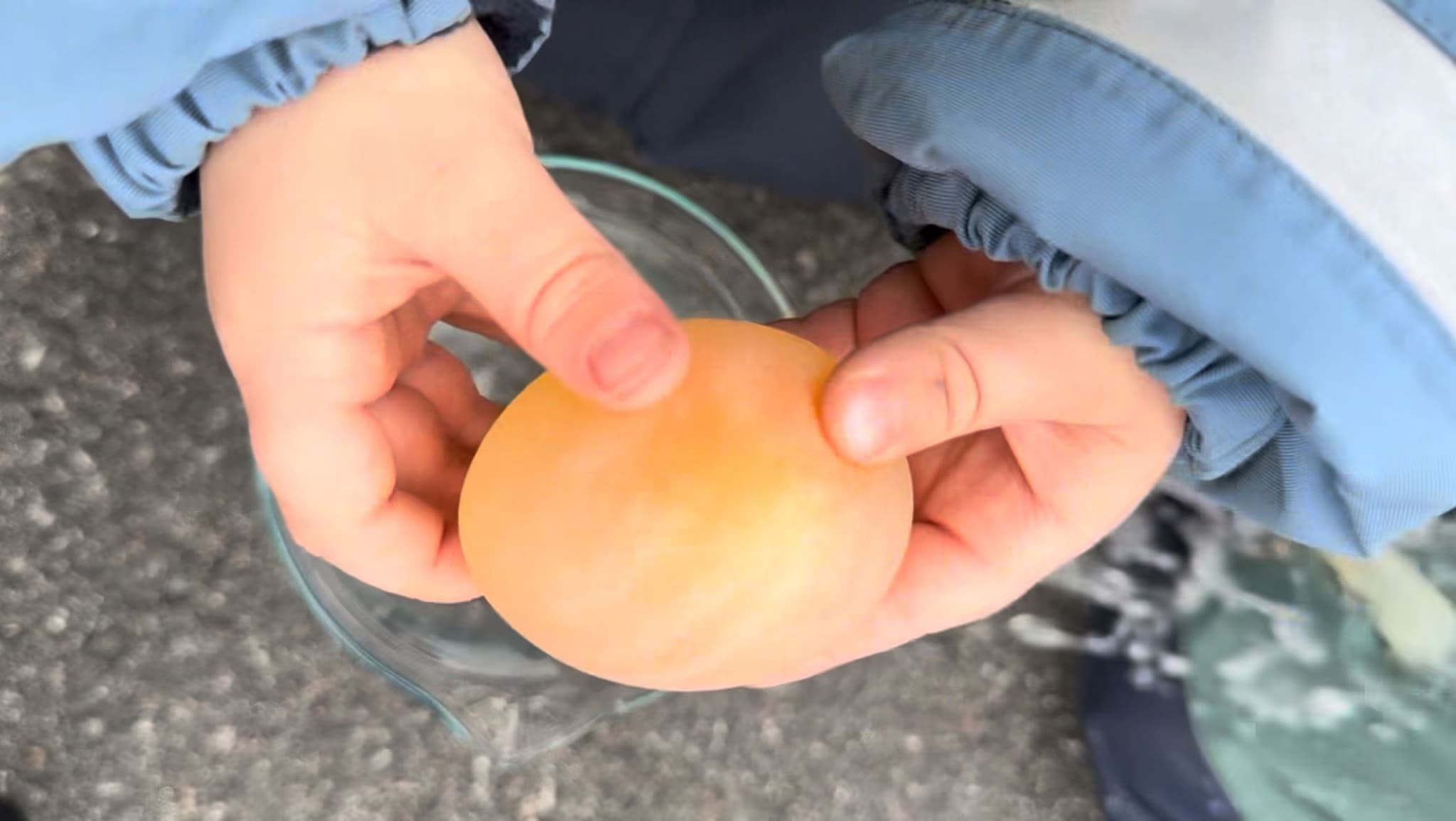 a child is holding an egg in their hands over a glass .