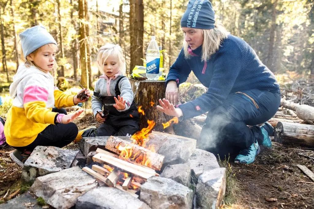 a woman and two children are sitting around a campfire in the woods .