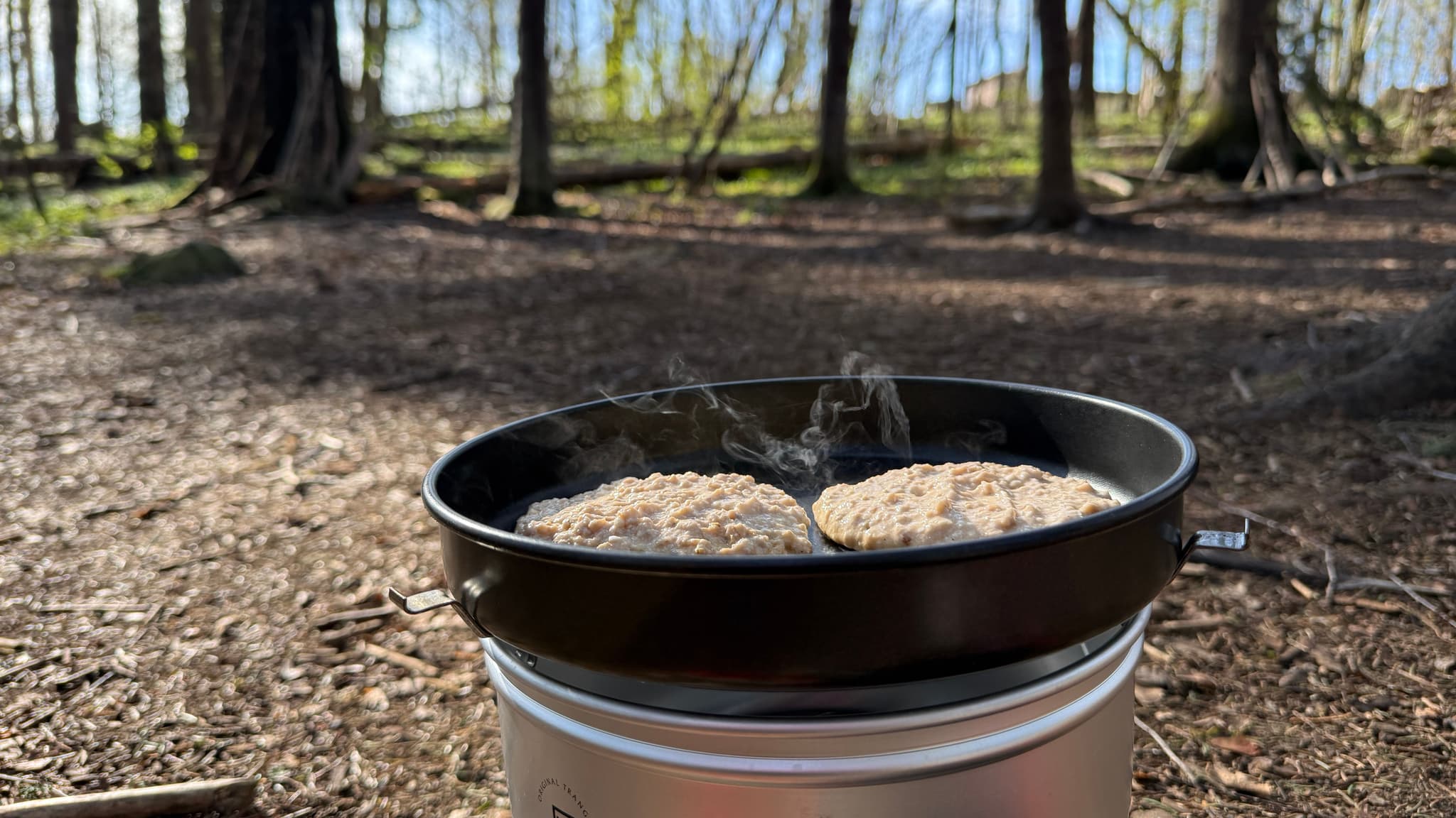 a pan of food is cooking on a stove in the woods .