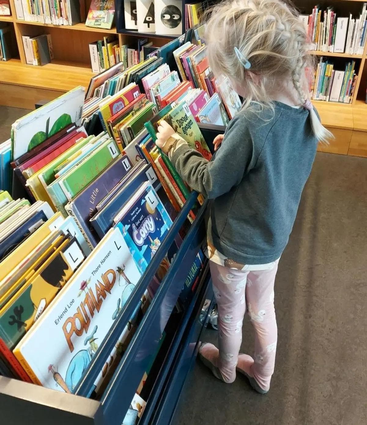 a little girl is looking at books in a library .