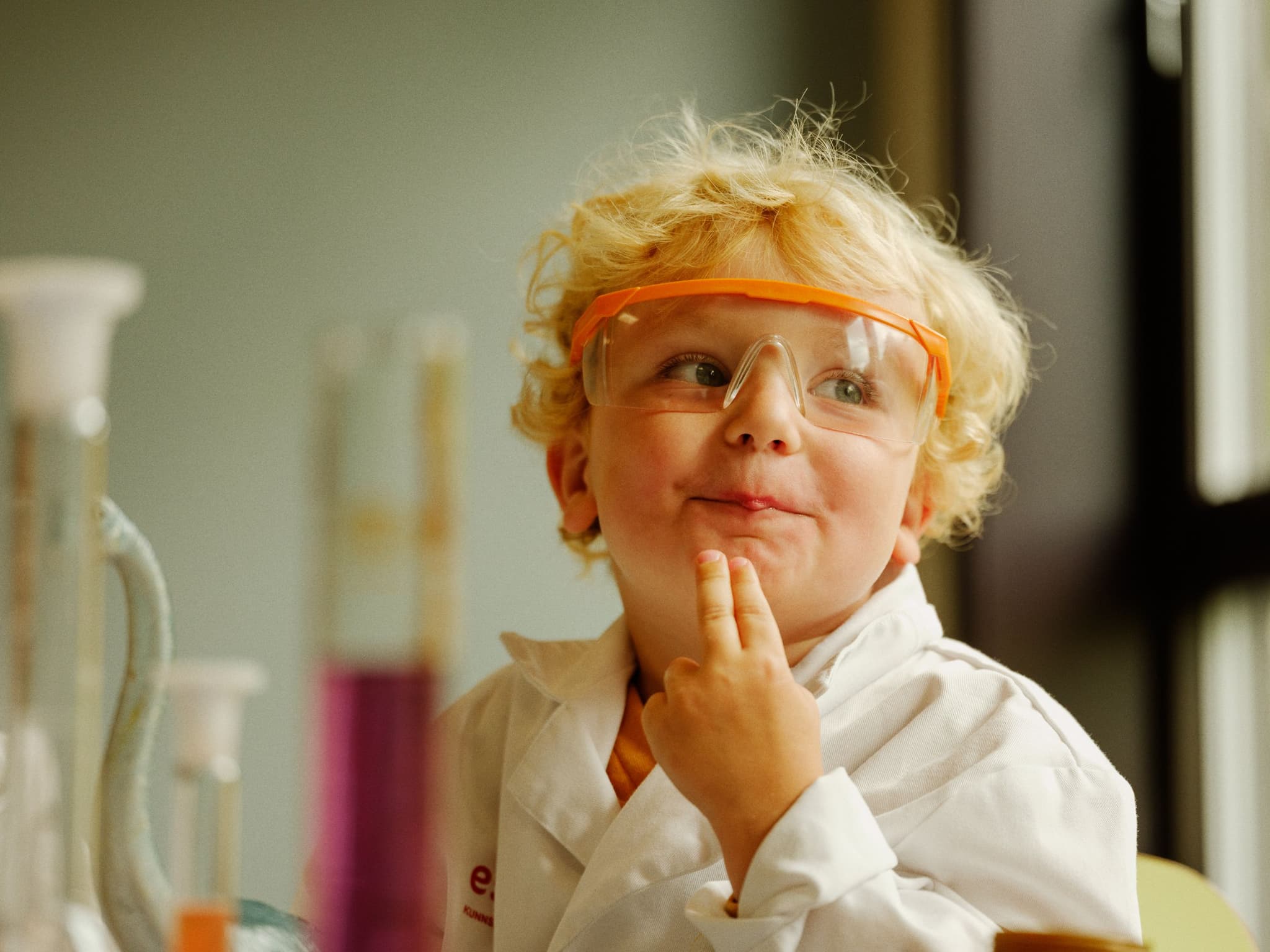 a young boy in a lab coat and goggles is making a funny face .